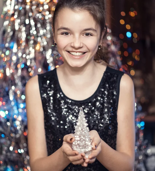 Young beautiful girl smiling and holding a Christmas tree. In black dress happy. — Stock fotografie