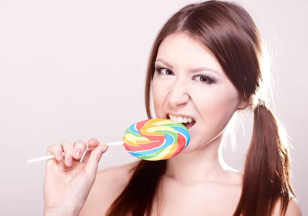 Beautiful girl with brown hair, glamorous make-up, fashion style portrait, eats candy sexy look on a gray background, smooth skin, — Stock Photo, Image