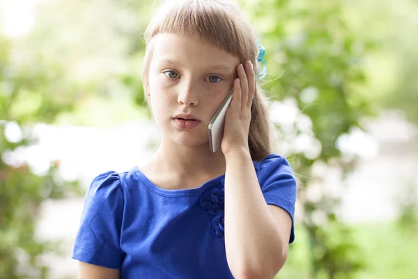 Маленькая девочка в летнем парке разговаривает по телефону, в синем платье. Blonde — стоковое фото