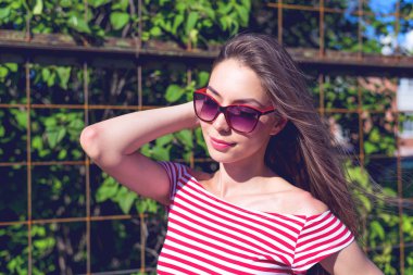 Beautiful girl in a bright red T-shirt, fashion lifestyle, posing against the backdrop of fence with green leaves
