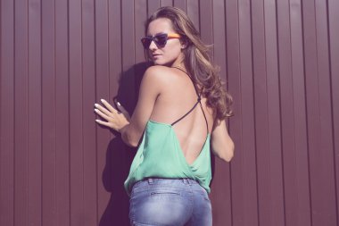 Beautiful girl in a light blouse and denim shorts, fashion stylish glasses stands on against the fence