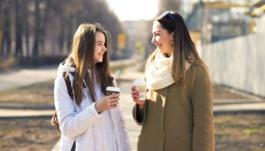 Mother and daughter talking, laughing smiling on the street, drinking coffee in cups