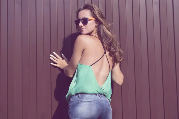 Beautiful girl in a light blouse and denim shorts, fashion stylish glasses stands on against the fence — Stok fotoğraf