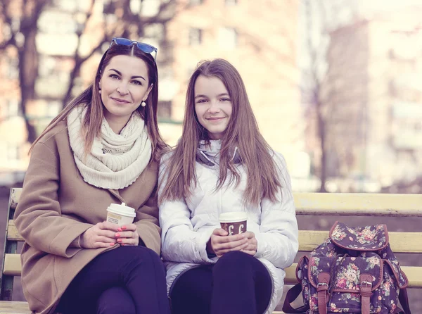 Matka i córka siedzi jesienią lub wiosną Park ławce, są trzymane w rękach filiżanek kawy — Zdjęcie stockowe