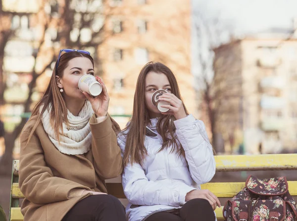 Madre e hija sentadas en otoño o primavera el parque en un banco al aire libre, beber café —  Fotos de Stock