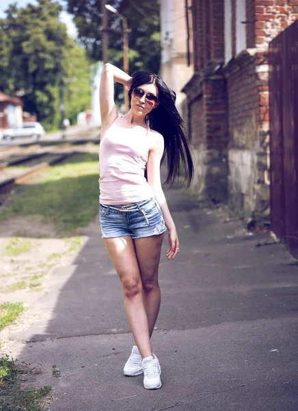 Jeune belle fille posant une ville de la mode en short en denim, chemisier et lunettes de soleil femme sexy — Photo