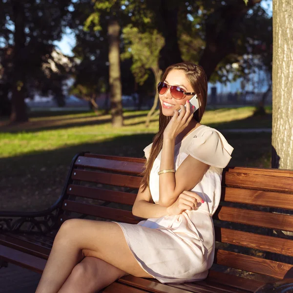 Gyönyörű érzelmi barna lány nevetett telefon park nyári szemüveg rózsaszín ruha, élvezze a nyaralást a város — Stock Fotó