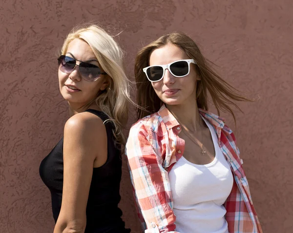 Duas meninas posando em uma parede de fundo marrom, óculos, loira e morena — Fotografia de Stock