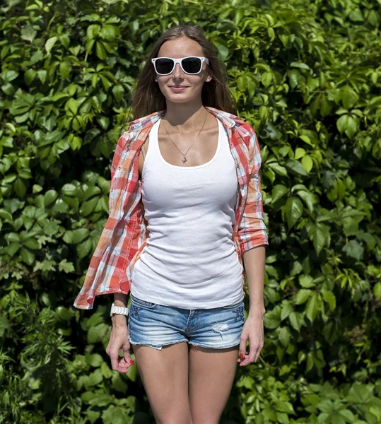 Brillante sexy, bella ragazza, indossando occhiali in posa di fronte a un verde cespugli da giardino , — Foto Stock