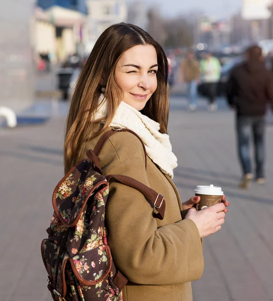Красивая брюнетка с сумкой и чашкой горячего чая или кофе, стоящая на улице — стоковое фото