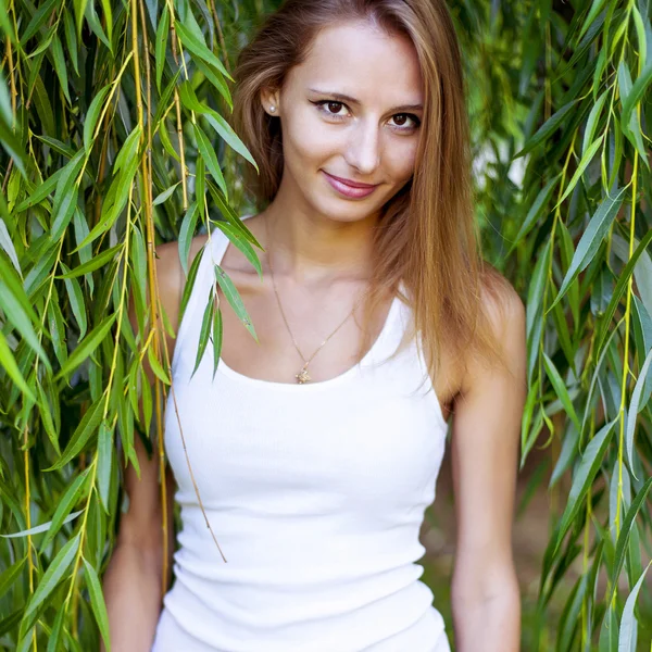 Felice bella giovane ragazza è tra le foglie di verde, occhiali, giorno d'estate all'aperto, sguardi sorridenti — Foto Stock
