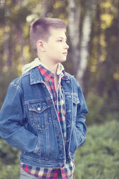 Niño se para parque pradera día soleado, chaqueta vaqueros, camisa mira a la distancia —  Fotos de Stock