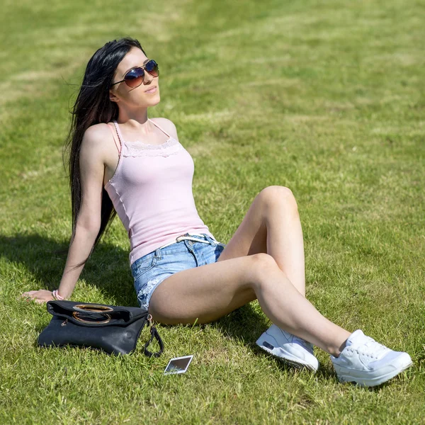 Mooi jong meisje zonnebaden op het gras, ontspannen na het werk, gooien telefoon en zak opzij, — Stockfoto