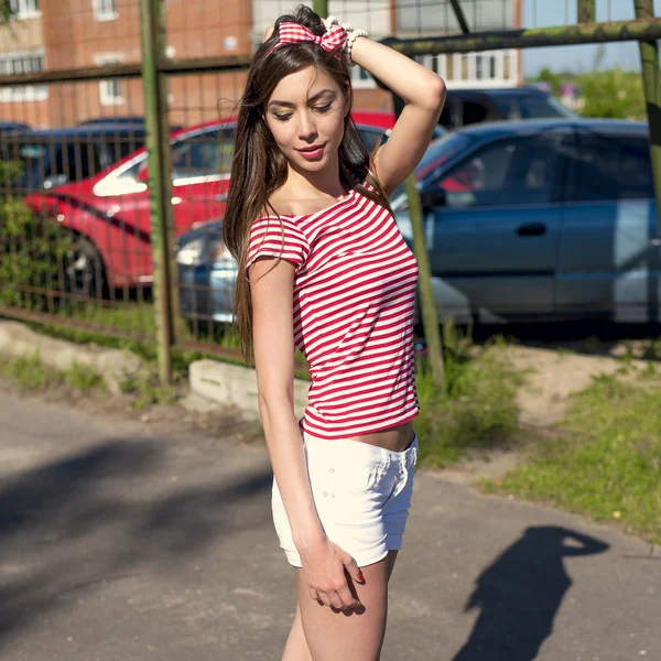 Menina bonita ao ar livre no parque infantil, descansando em uma camiseta vermelha brilhante shorts brancos — Fotografia de Stock