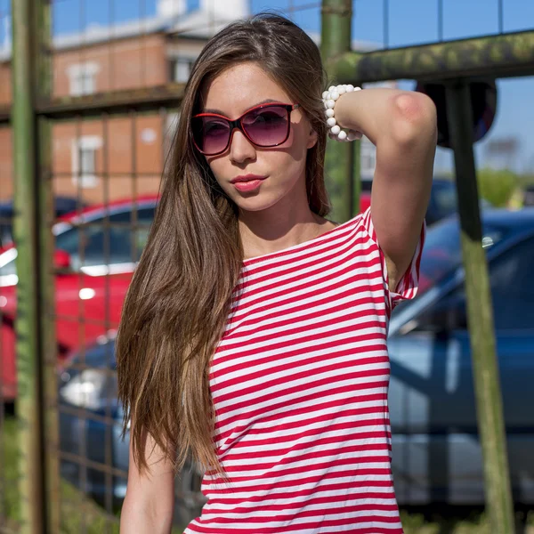 Beautiful young woman, outdoors, resting in a bright red T-shirt, fashion style, adjusting happy brunette hair — Stockfoto