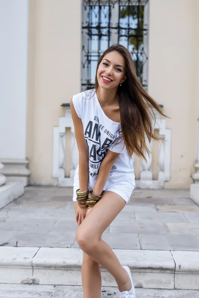 Belle jeune fille brune posant dans une ville ensoleillée journée d'été, en short blanc, T-shirt, repos heureux, style mode, bronzé avec des cheveux longs. Profiter de la  . — Photo