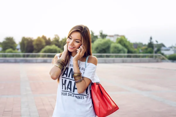 Schöne junge Frau am Telefon in weißer Bluse und kurzen Hosen, lange Haare, brünett, glücklich lächelnd. Soziale Netzwerke, Online-Chat. Mode, Stil, Leben Stadt. — Stockfoto