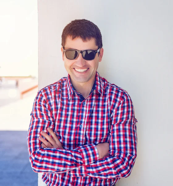 The man in the summer against the wall, glasses, happy smiles, wearing jeans and a shirt,  bright sunny day. The idea of the concept   businessman in the city. Lifestyle, portrait   successful  close — Stock Photo, Image