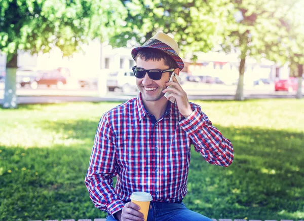 man in  shirt and jeans  glasses, talking on the phone,  smartphone, the concept of summer,  businessman  vacation. City lifestyle.  the street in the park. Happy smiling, emotional. In his hand  mug