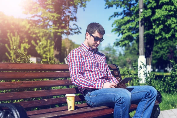 Mann in Hemd und Jeans Sonnenbrille, Video-Looks auf dem Tablet entsprechen den sozialen Netzwerken, im Sommer der Bank, dem Konzept des Geschäftsmannsurlaubs. Lebensstil in der Stadt. die Straße in der — Stockfoto