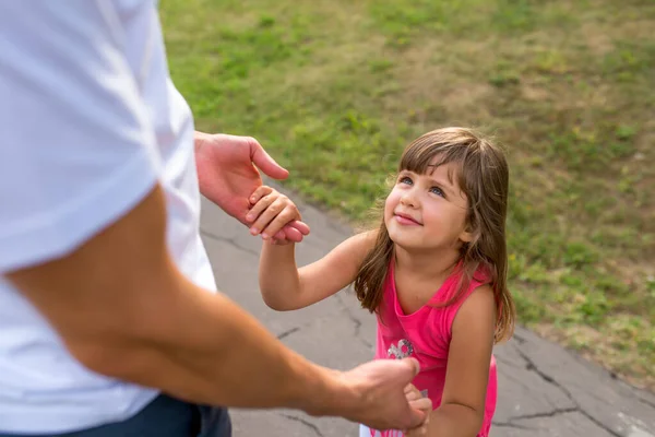 Мужчина папа держит за руки ребенка, маленькая девочка, счастливая, веселится и улыбается, со своей дочерью летом в городском парке. Девочка 5-7 лет, отдыхающая в выходные на прогулке. — стоковое фото