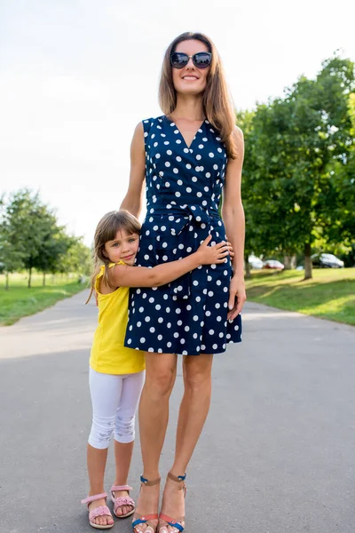 Kobieta mama spaceruje z córką latem w parku miejskim. Mała dziewczynka 5-7 lat, przytula swoje mumu, szczęśliwy uśmiech raduje się i odpoczywa w weekend na spacer. Zdjęcie Stockowe