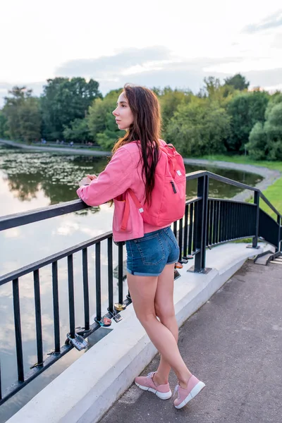 Wanita di musim panas di kota dekat danau, kolam sungai, melihat pemandangan, ransel merah muda di belakangnya. Relaksasi setelah bekerja, menikmati alam. — Stok Foto
