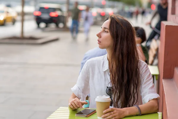 Beautiful woman sits in street cafe, listens voice message online application on Internet, city, waiting friends, meeting date. Free space for a copy of text. Cup with coffee, tea, breakfast, lunch. Obrazek Stockowy