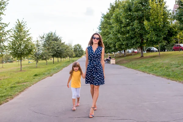 Žena maminka procházky s malou holčičkou dcera 5-7 let, v létě v městském parku, ležérní oblečení a šaty, happy walk, úsměv a relax o víkendu. — Stock fotografie