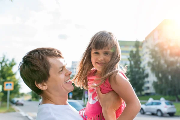 Pria ayah mengambil gadis, putri 5-6 tahun, di musim panas di kota, tersenyum gembira gembira dan bersenang-senang. Konsep keluarga bahagia, hari ayah. Istirahat akhir pekan. Latar belakang jalan dan mobil. — Stok Foto