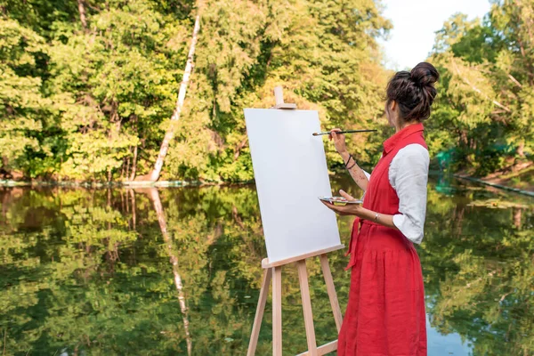Ruang kosong untuk teks, wanita seniman taman musim panas dekat danau, kolam sungai, menarik gambar, kanvas putih. Kreativitas kreasi, fantasi seni. Cermin refleksi dalam air, gadis cat kuas berwarna. — Stok Foto
