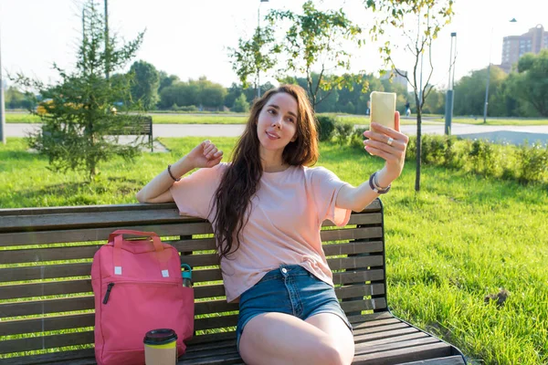 Mujer en verano en un parque de la ciudad grabación de vídeo en línea en el teléfono, la radiodifusión de aplicaciones de redes sociales en Internet, descansando después del trabajo. Fondo de hierba verde. Fotos de stock libres de derechos