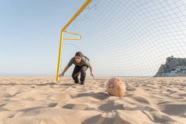 Young teenage goalkeeper on a beach soccer team prepares to dive to stop the ball.