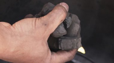 Adamın eli kavrulmak için bir fıçının içine kömür koyuyor.
