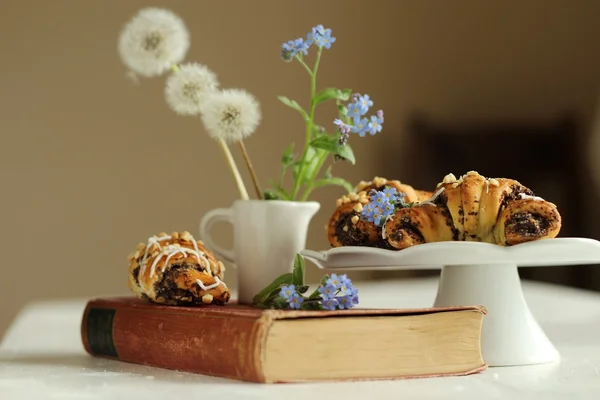 Krug mit Blumen vergiss-mich-nicht auf Vintage-Buch und Croissants — Stockfoto
