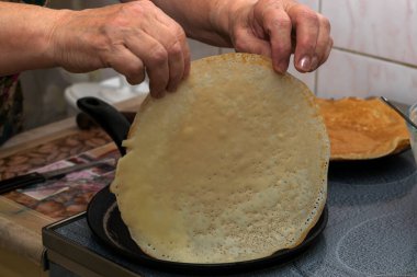 Kadının elleri krep hamurunu sıcak bir tavaya döker ve her iki tarafta kızartıp elleriyle çevirir..