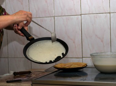 Kadının elleri krep hamurunu sıcak bir tavaya döker ve her iki tarafta kızartıp elleriyle çevirir..