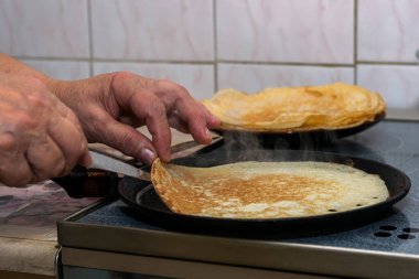 Kadının elleri krep hamurunu sıcak bir tavaya döker ve her iki tarafta kızartıp elleriyle çevirir..