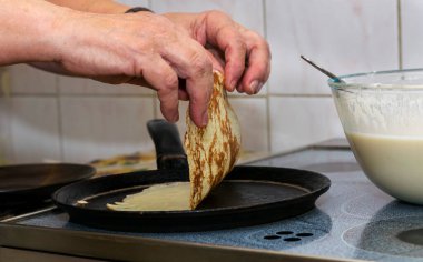 Kadının elleri krep hamurunu sıcak bir tavaya döker ve her iki tarafta kızartıp elleriyle çevirir..