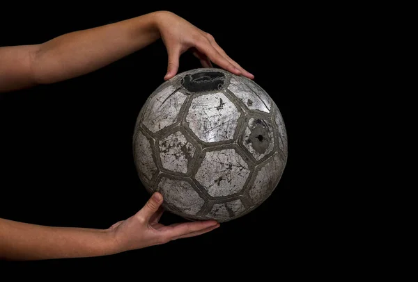 Old soccer ball in the hands of a teenager on a black background.