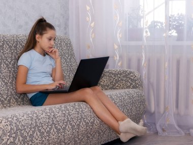 Genç bir kız kanepede oturuyor, çevrimiçi antrenman yapıyor ve not defterine bilgi yazıyor..