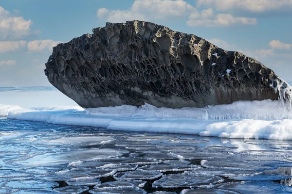晴れた日には雪に覆われた白い氷の流れと凍った岩が海から突き出ています — ストック写真