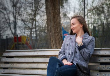 Genç, güzel bir kız güneşli bir öğleden sonra parkında bankta oturuyor.