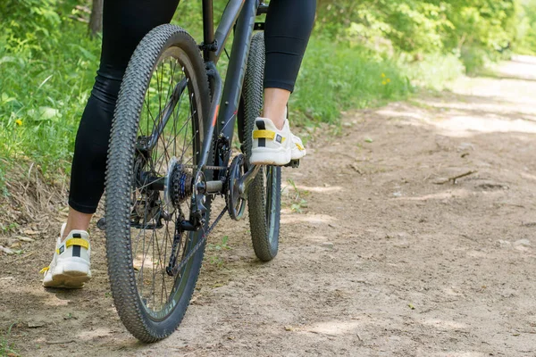 Une fille sur un vélo marche par une journée chaude ensoleillée dans le parc. Photo De Stock