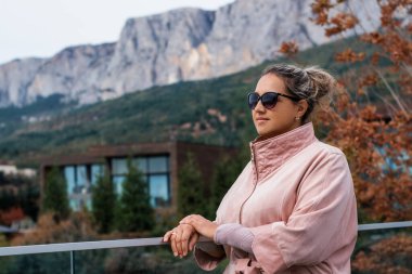 Pembe ceketli bir kadın açık havada korkulukların önünde duruyor mavi denizin arka planına karşı. .