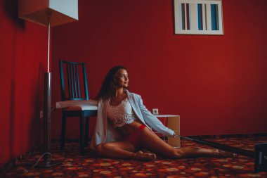 Beyaz ceketli ve kırmızı mayo giyen genç bir kız, kırmızı bir odada esneme ve denge ile meşgul mobilya ve zemin lambaları ile