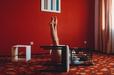 Beyaz ceketli ve kırmızı mayo giyen genç bir kız, kırmızı bir odada esneme ve denge ile meşgul mobilya ve zemin lambaları ile