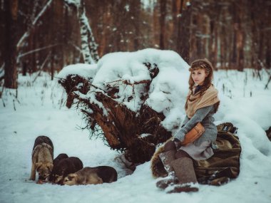 Genç bir kız, kışın bir çam ormanında yalnız başına keçeli çizme ve basit köylü kıyafetleri giyerek başıboş köpekleri beslemeye geldi.