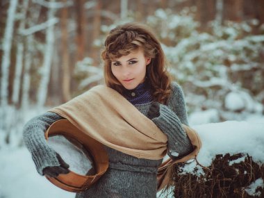 Genç bir kız, kışın bir çam ormanında yalnız başına, keçeli çizme ve basit köylü kıyafetleri giyiyor.