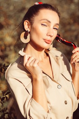 Yüzünde güzel makyajlı, etkileyici yüz hatları ve vücudu olan güzel esmer bir kız. Sonbaharda güzel ağaçların arasında şık bir takım elbise giyiyor.